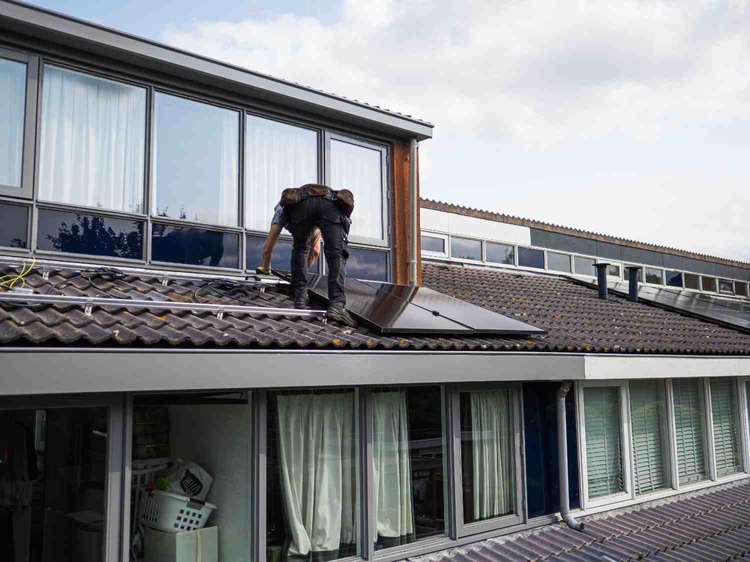 A professional clean-energy technician installing high-efficiency solar panels on the roof of a luxury modern residential property in Bulimba.