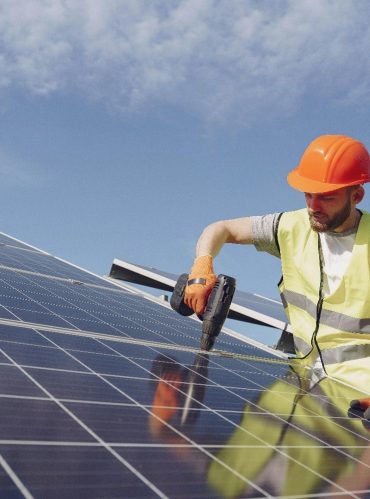 Professional solar maintenance technician in a high-visibility vest inspecting a rooftop solar panel system array.